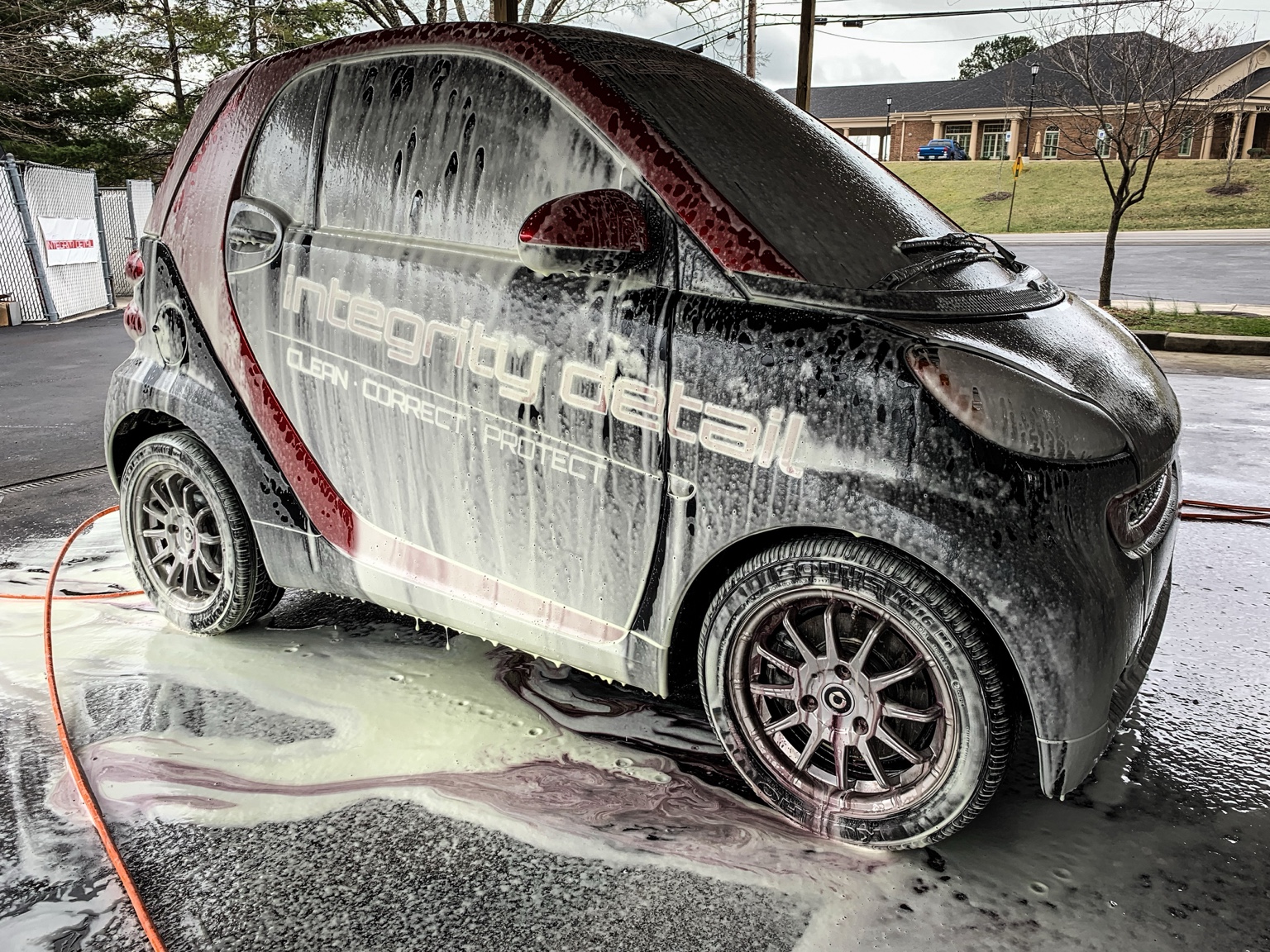 Integrity Detail branded Smart car covered in wash foam during exterior detailing at the shop