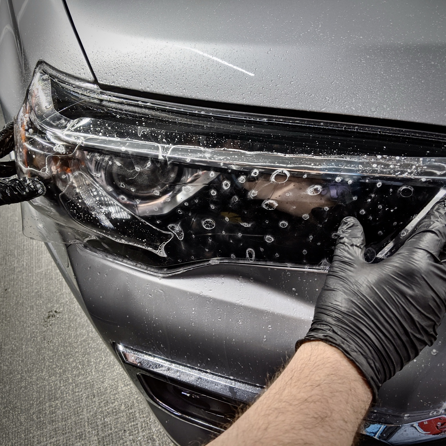 Clear protective film being fitted to a silver vehicle headlight at Integrity Detail