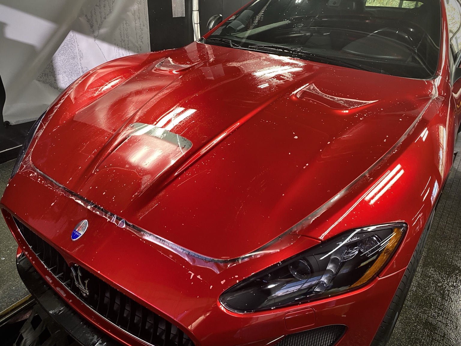 Clear paint protection film being fitted across the red Maserati hood during installation at Integrity Detail