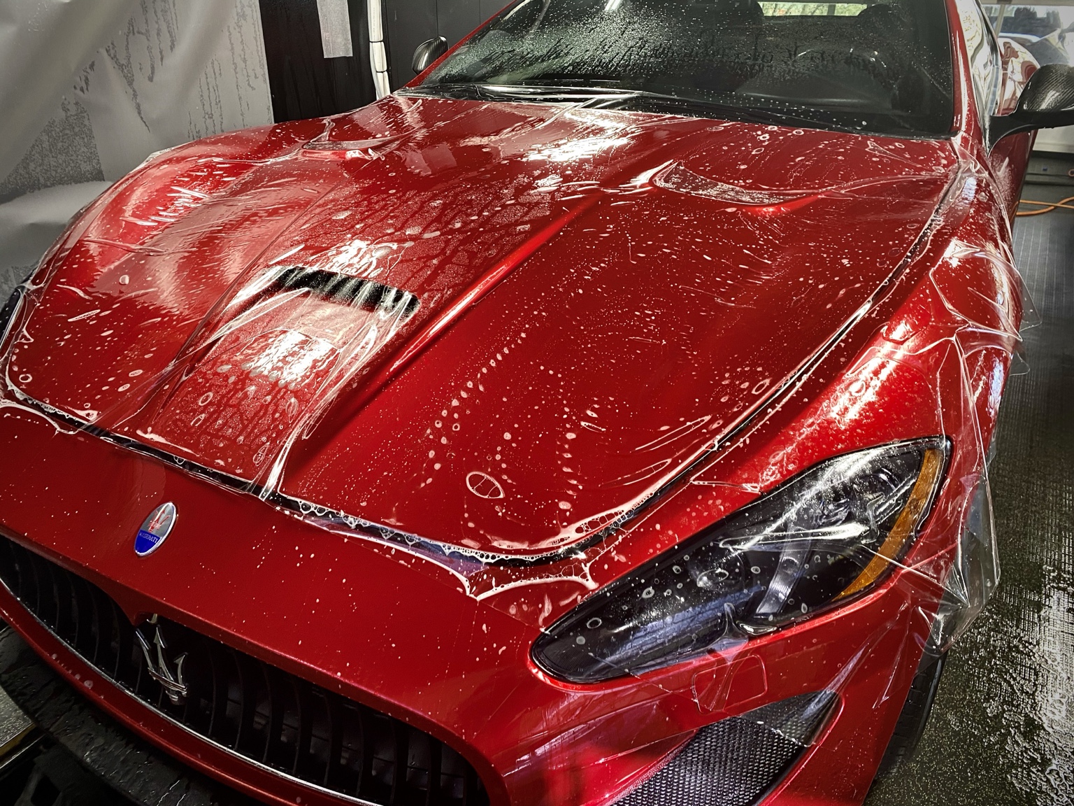Actual Integrity Detail installation of clear paint protection film on a red Maserati, with film being positioned across the hood and front end